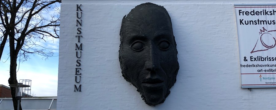 Mørk maske af ansigt der hænger på hvid væg
