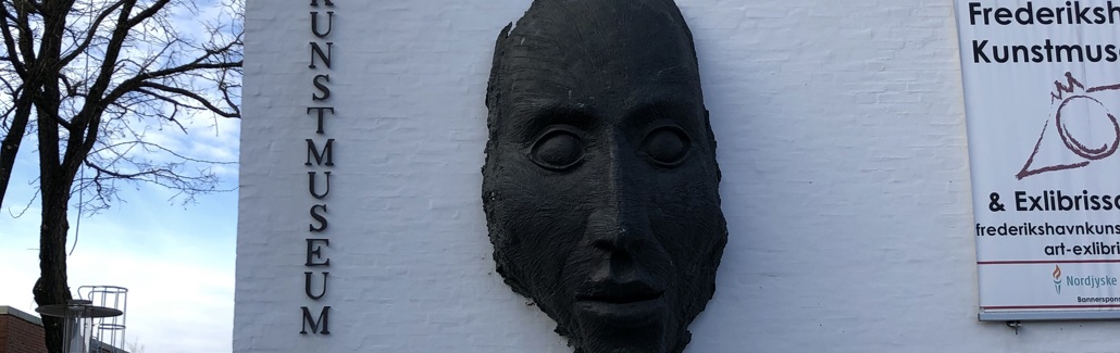 Mørk maske af ansigt der hænger på hvid væg