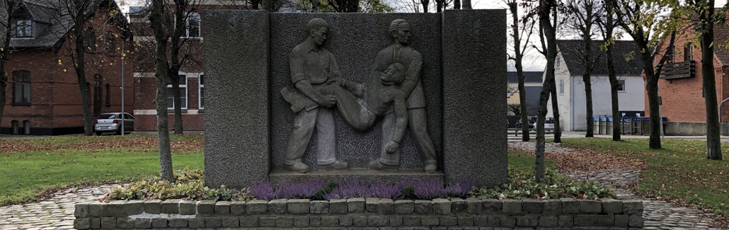 Firkantet granitmonument med to mænd der løfter en såret kammerat