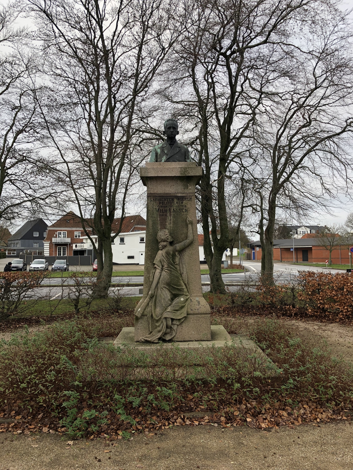 Buste af mand på høj granitsokkel med kvinde i kjole