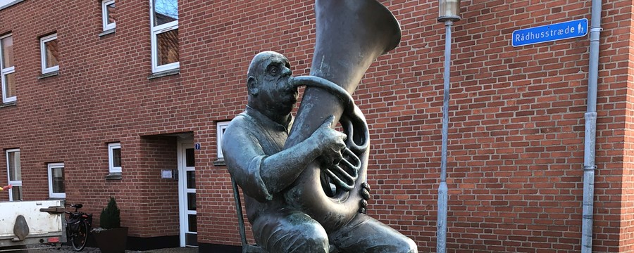 Bronzeskulptur af siddende mand der spiller tuba