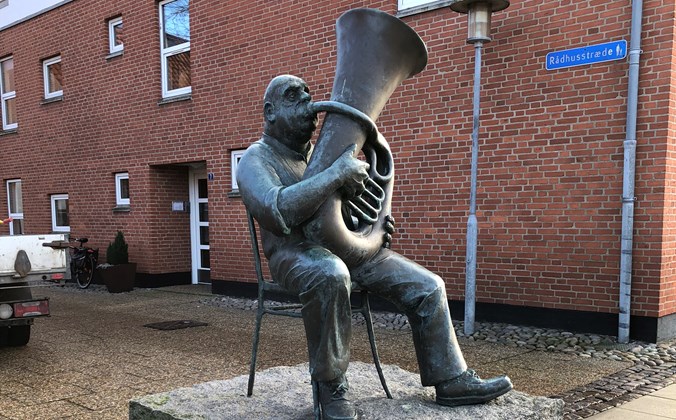 Bronzeskulptur af siddende mand der spiller tuba
