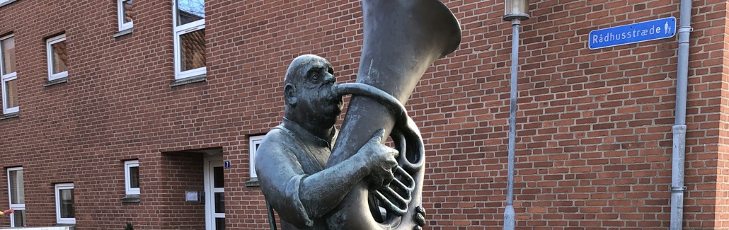 Bronzeskulptur af siddende mand der spiller tuba