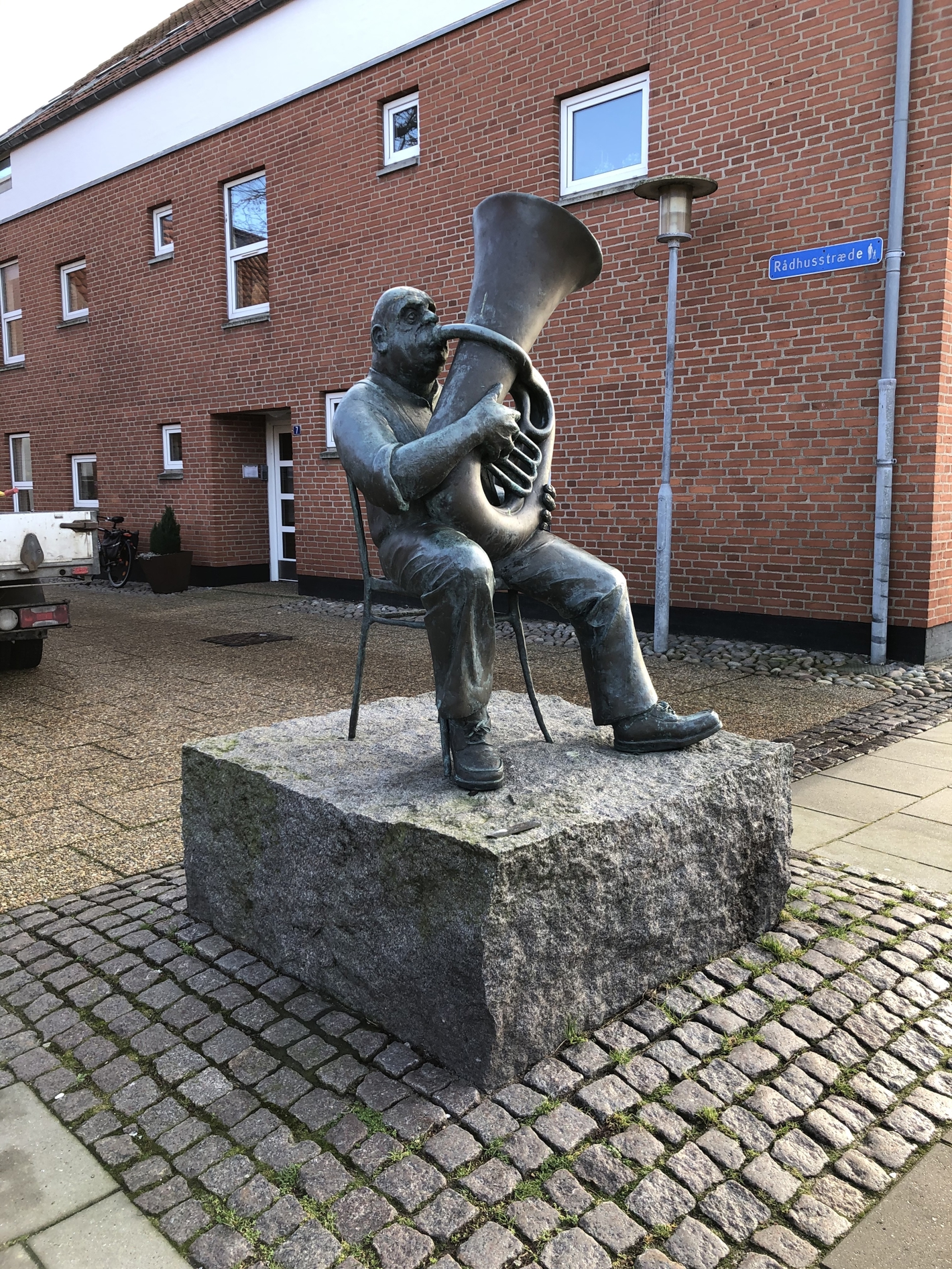 Bronzeskulptur af siddende mand der spiller tuba