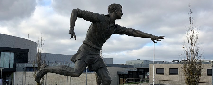 Bronzeskulptur af fodboldspiller på firkantet granitsokkel