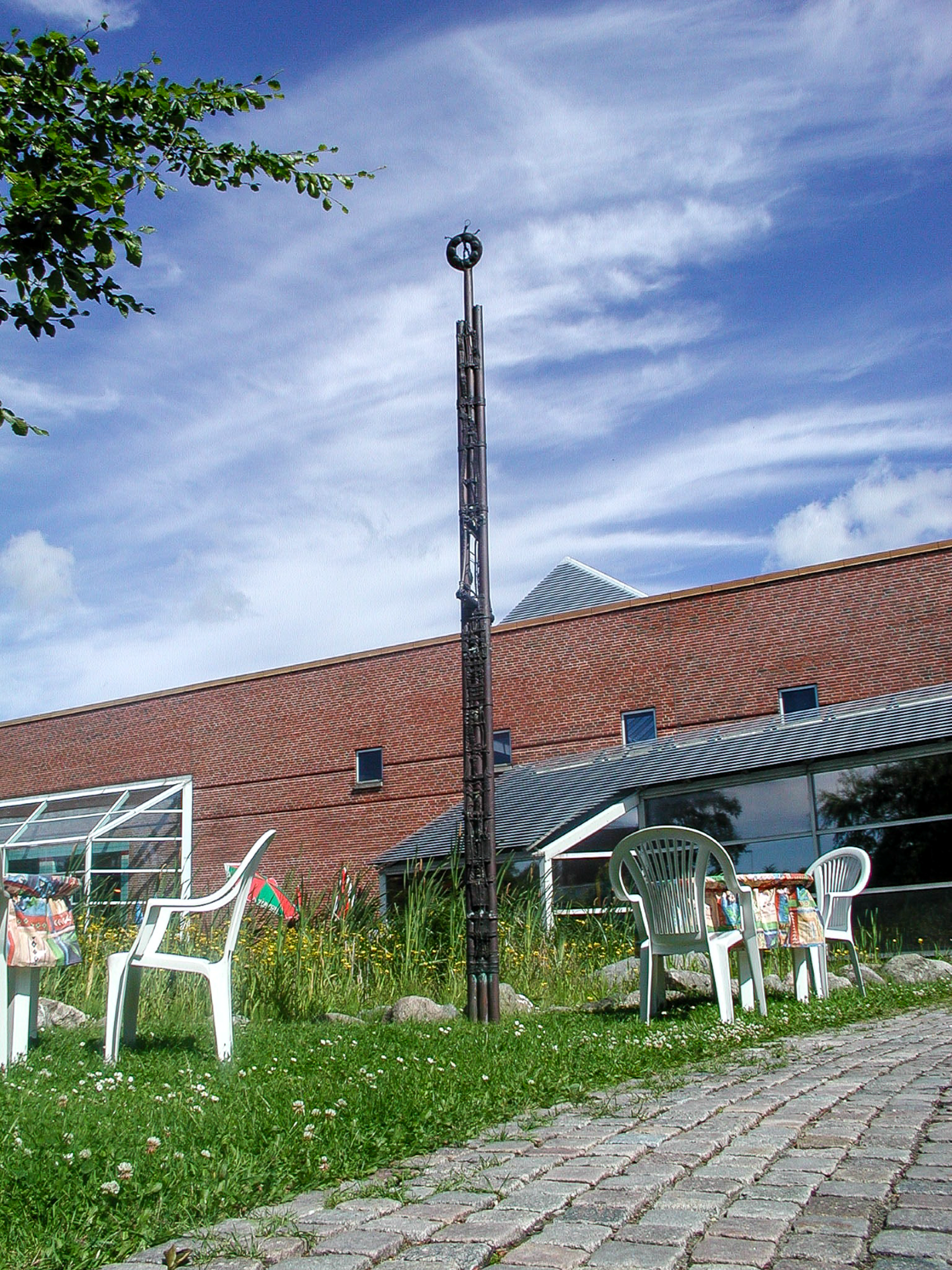 Høj metalsøjle med figurer og en sol på toppen