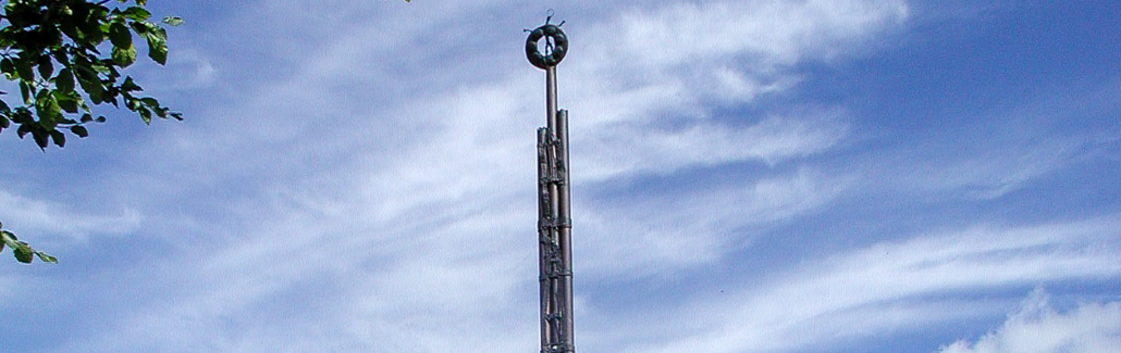 Høj metalsøjle med figurer og en sol på toppen