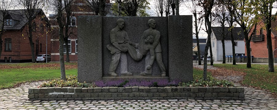 Firkantet granitmonument med to mænd der løfter en såret kammerat