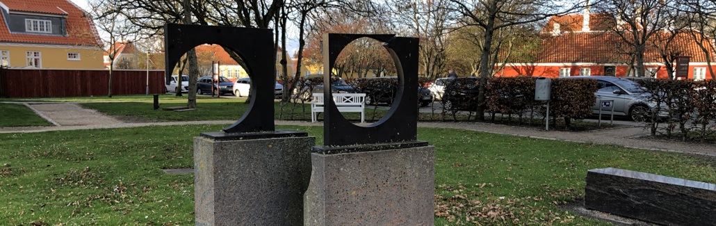 Firkantede metalskulpturer med runde huller på stensokkel