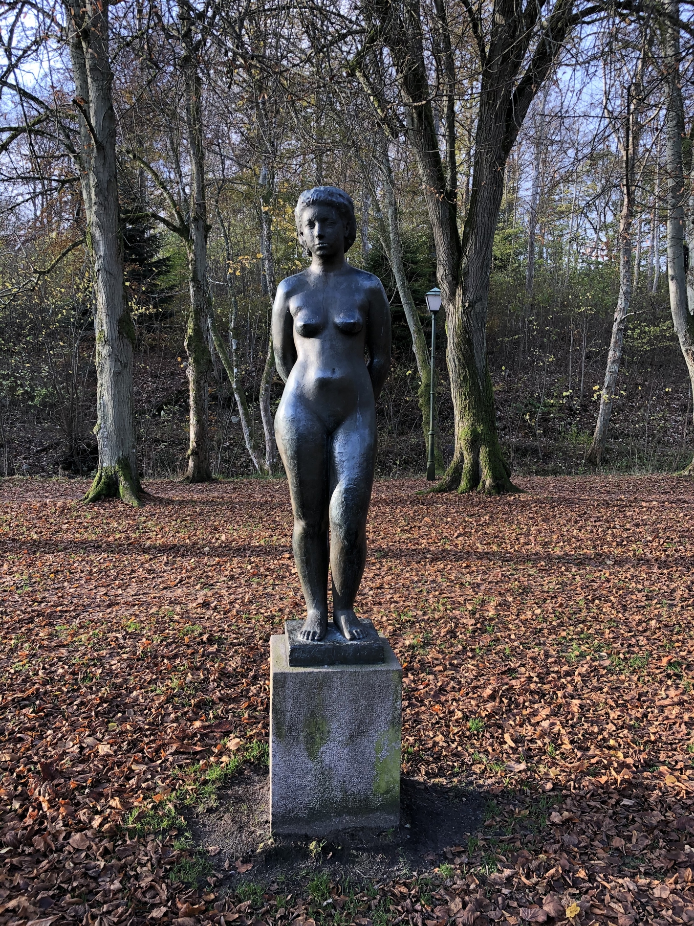 Bronzeskulptur af nøgen kvinde med hænderne på ryggen